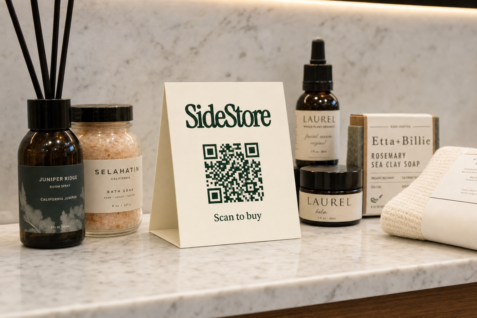 A marble countertop displays beauty and wellness products including a room spray, bath soak, facial serum, balm, and rosemary sea clay soap,