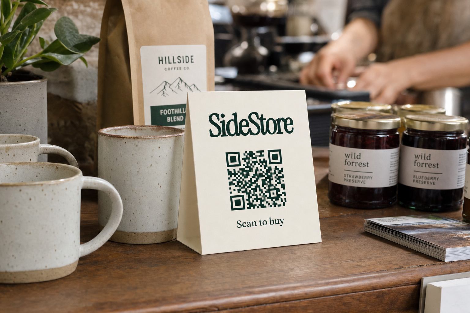 A wooden counter displays ceramic mugs, a Hillside Coffee Co bag, jars of Wild Forrest preserves, and a SideStore sign with a QR code