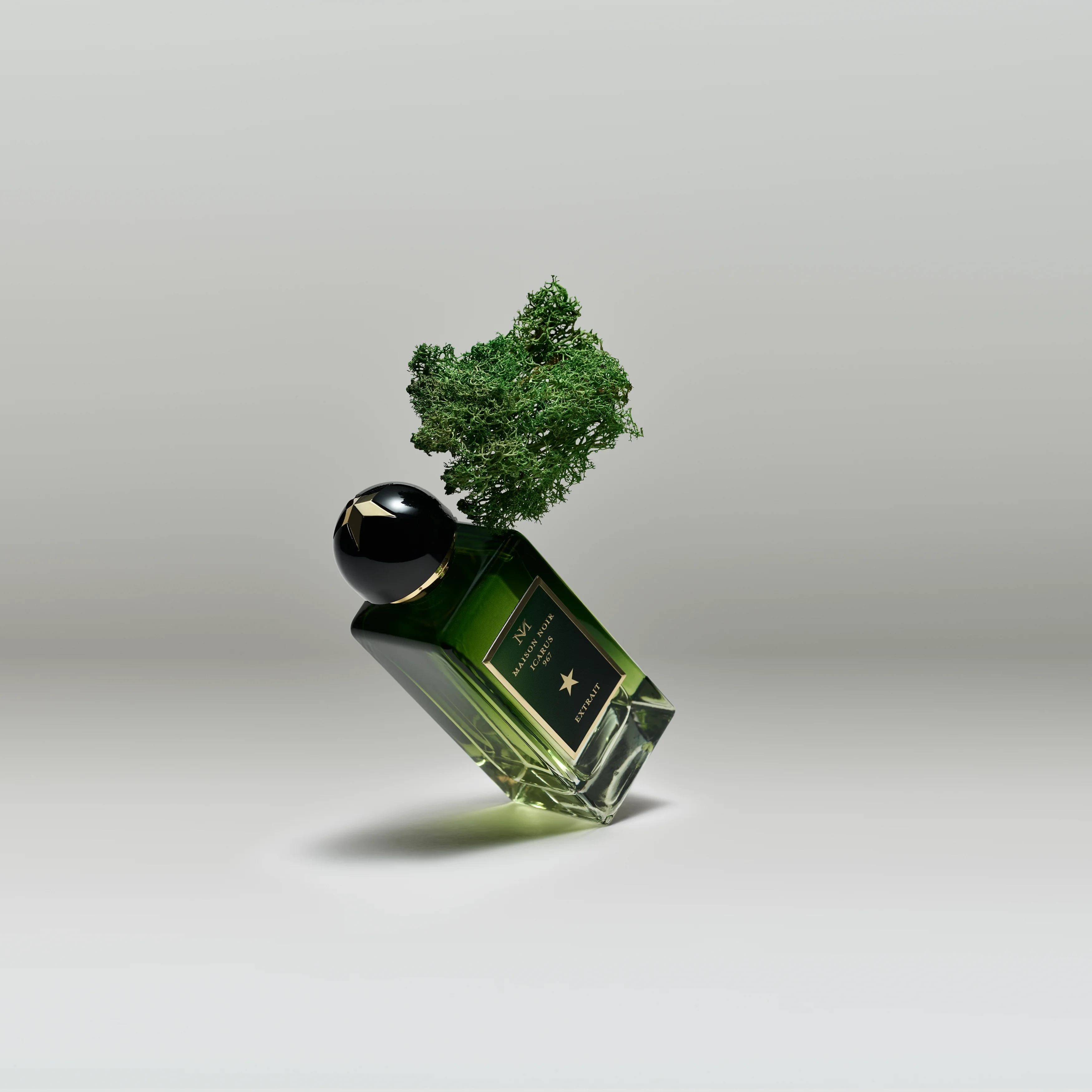 A flacon balanced against a clump of green moss on a pale grey ground, oakmoss being a pillar of the fougere accord