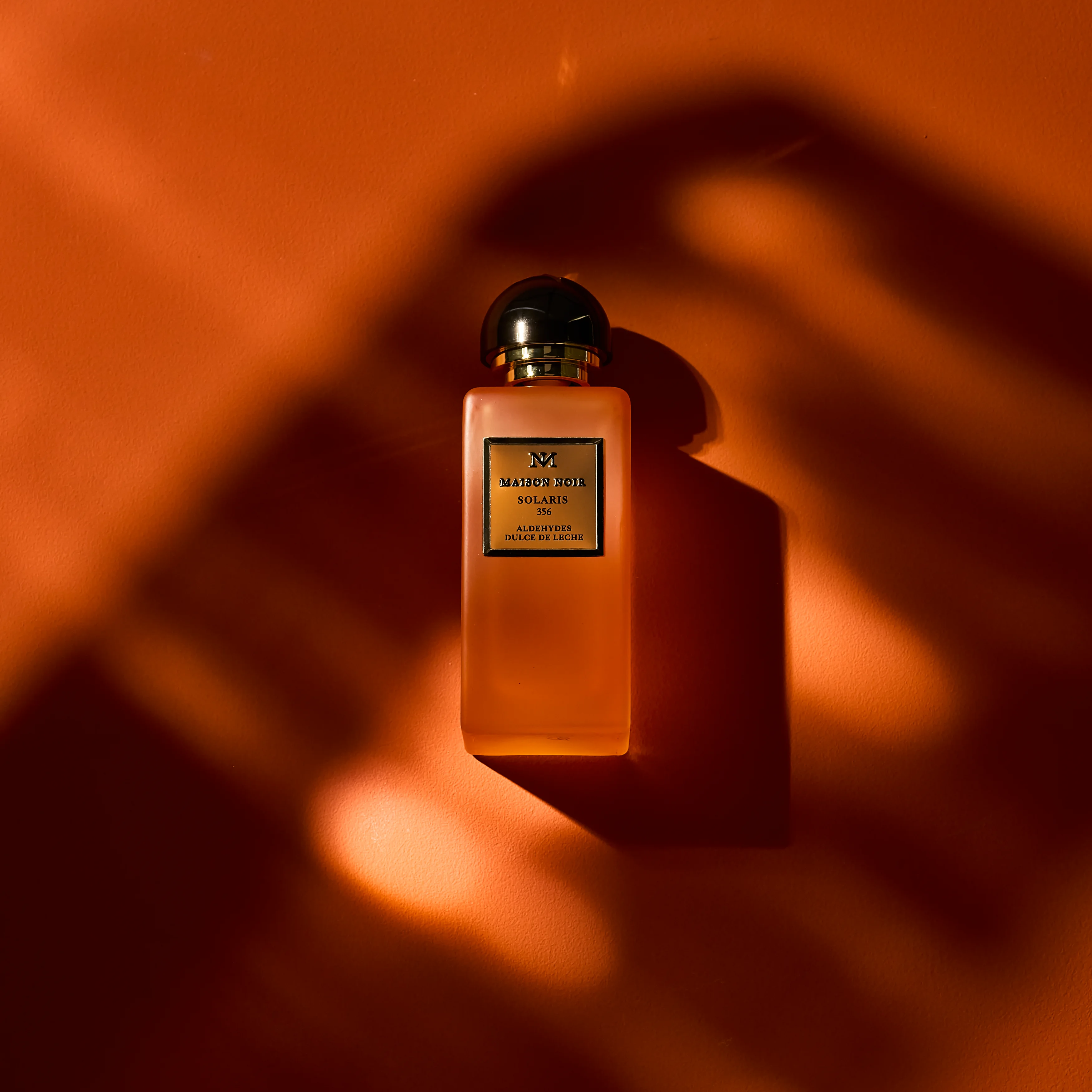 A Maison Noir flacon on a warm terracotta ground under hard low sun